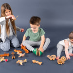 Three kids of various ages playing on the floor with wooden airplanes, cars and baby toys.