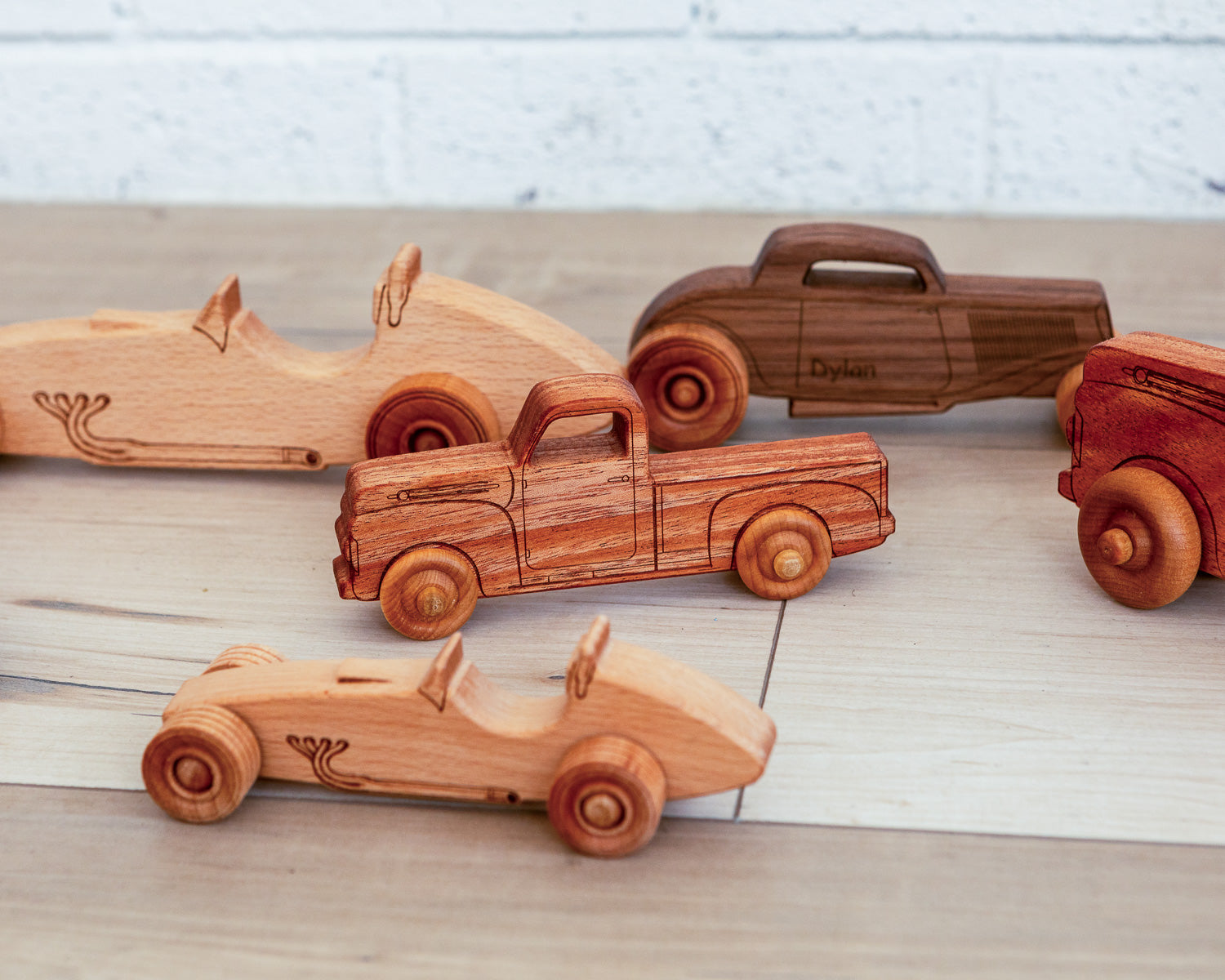 Various wooden race cars, pickup trucks and hot rods made from different sustainably sourced wood sitting on the floor. 