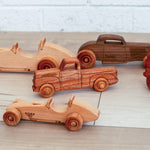 Various wooden race cars, pickup trucks and hot rods made from different sustainably sourced wood sitting on the floor. 