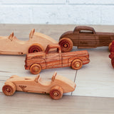 Various wooden race cars, pickup trucks and hot rods made from different sustainably sourced wood sitting on the floor. 