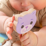 A baby holding a wooden cat rattle.