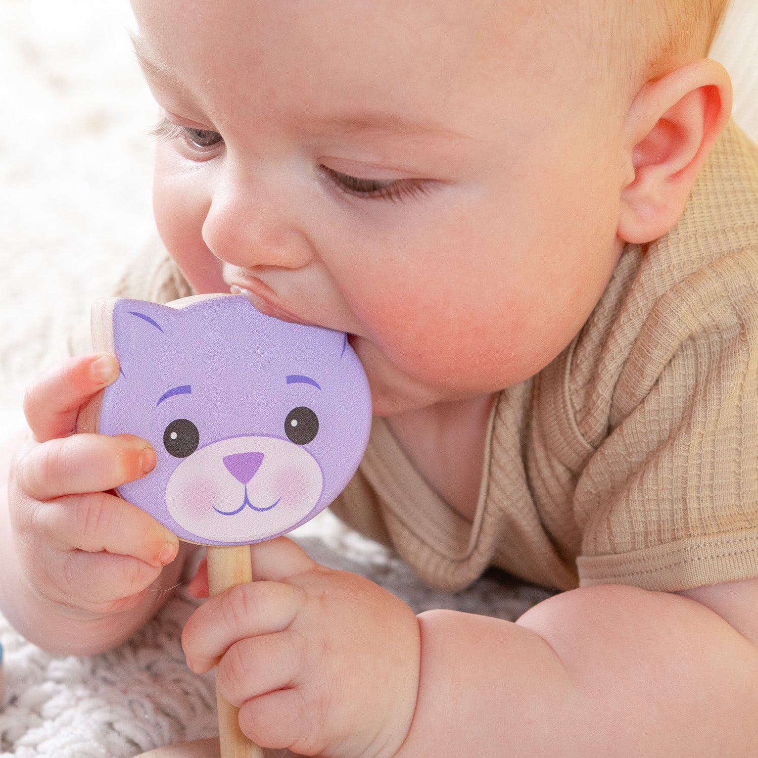 A baby teething on a wooden cat rattle.