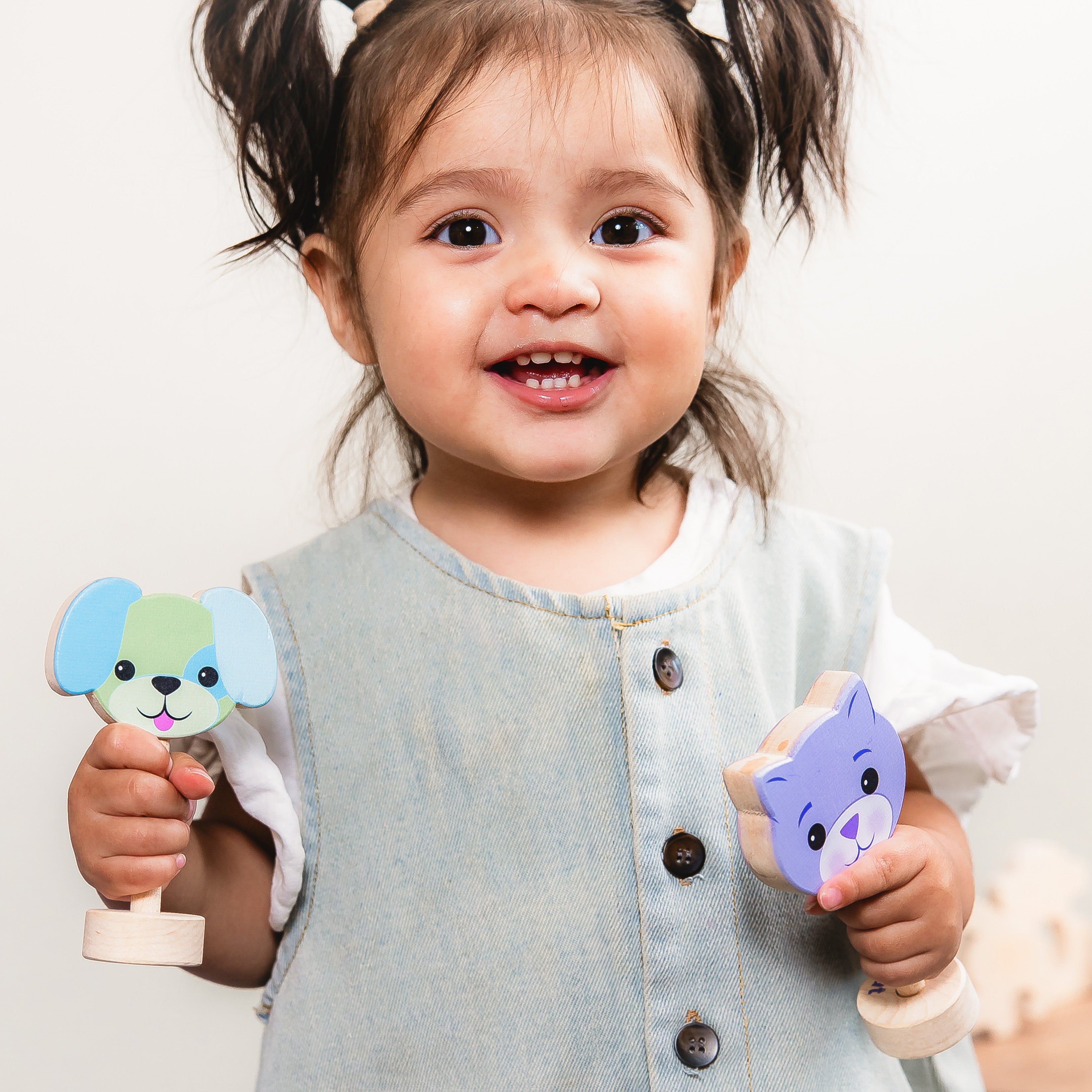 Child holding wooden toys with animal faces against a plain background
