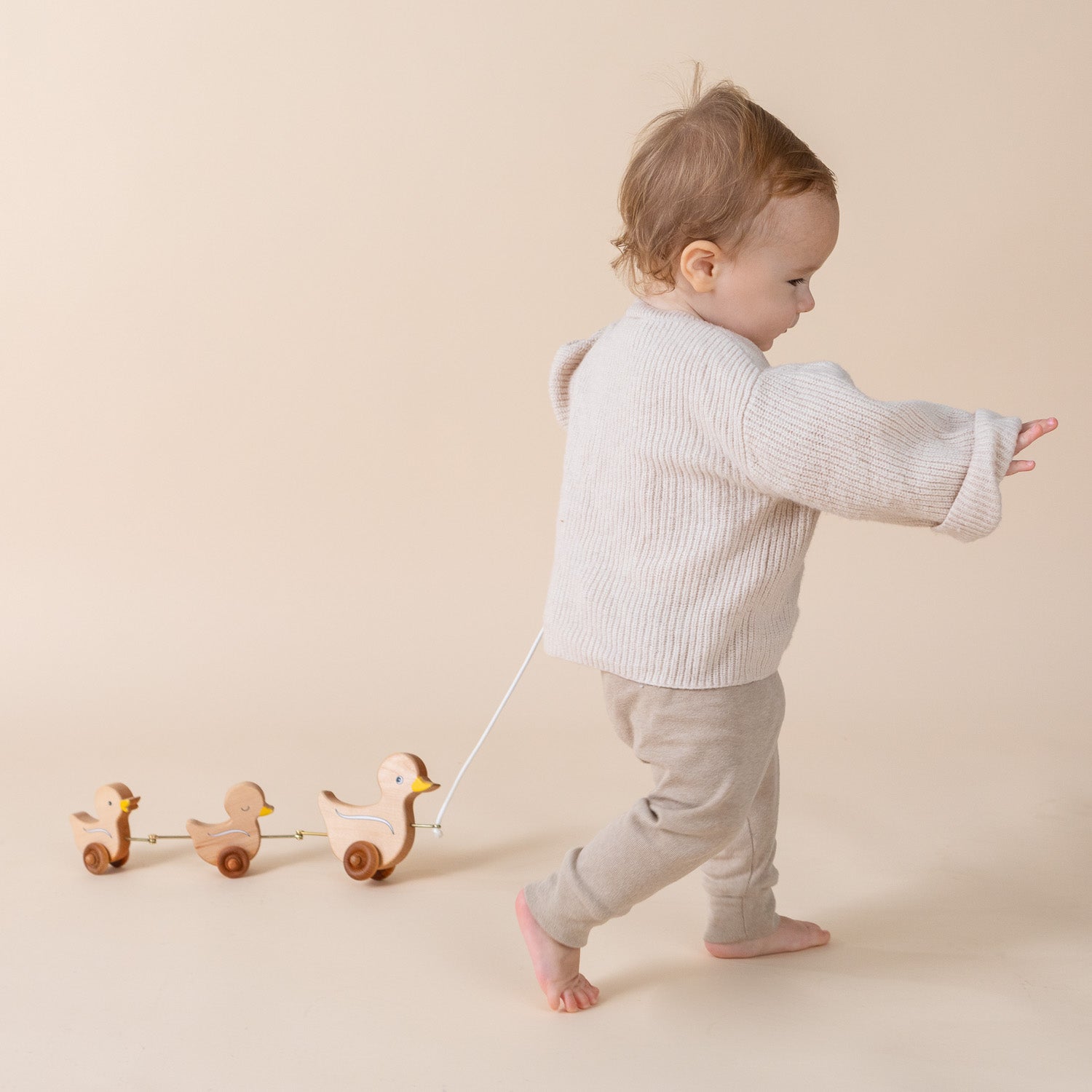 A toddler pulling our pull behind toy of three duck with a string. 
