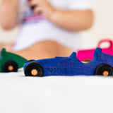 Blue toy car on a white surface with blurred children playing in the background