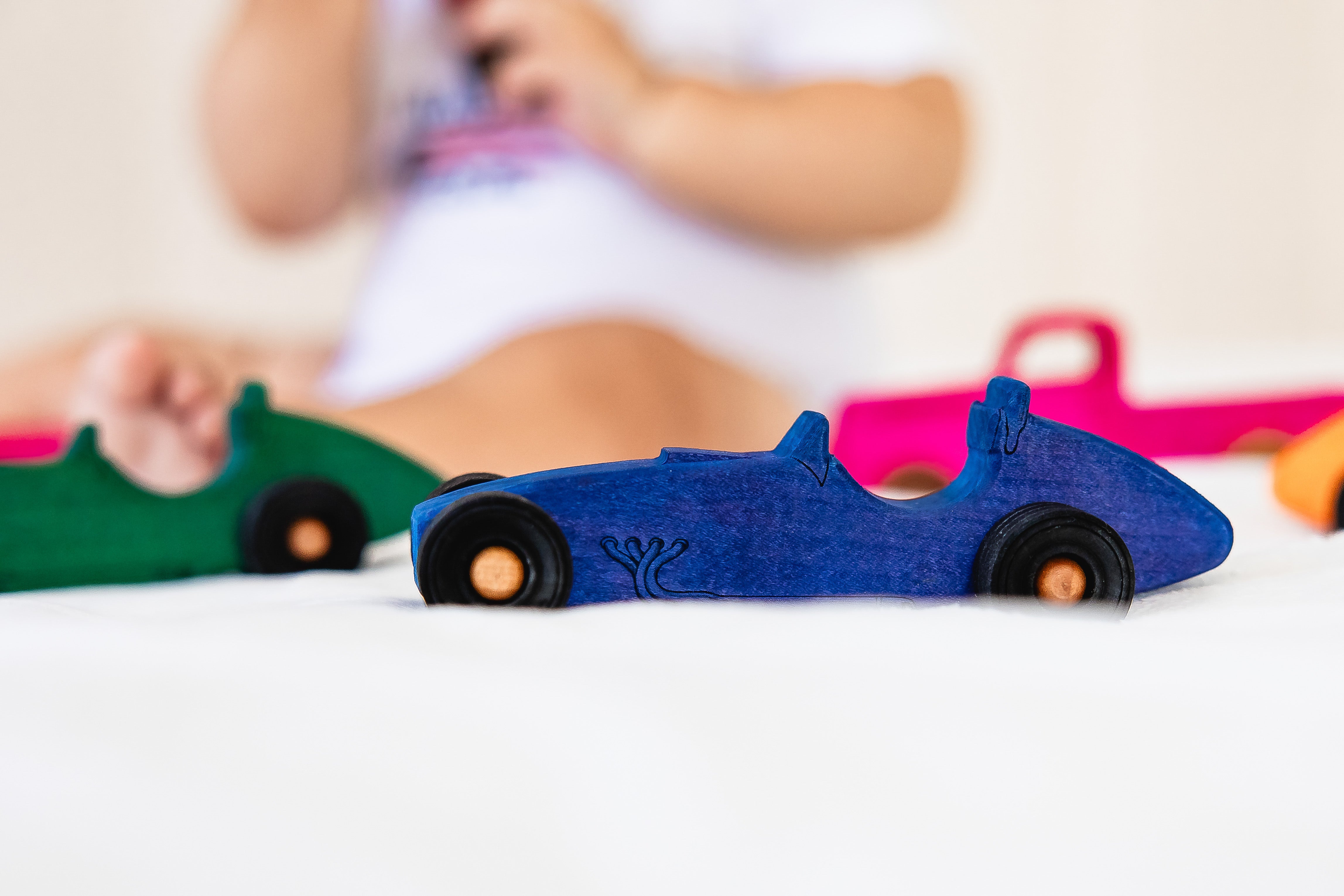 Blue toy car on a white surface with blurred children playing in the background