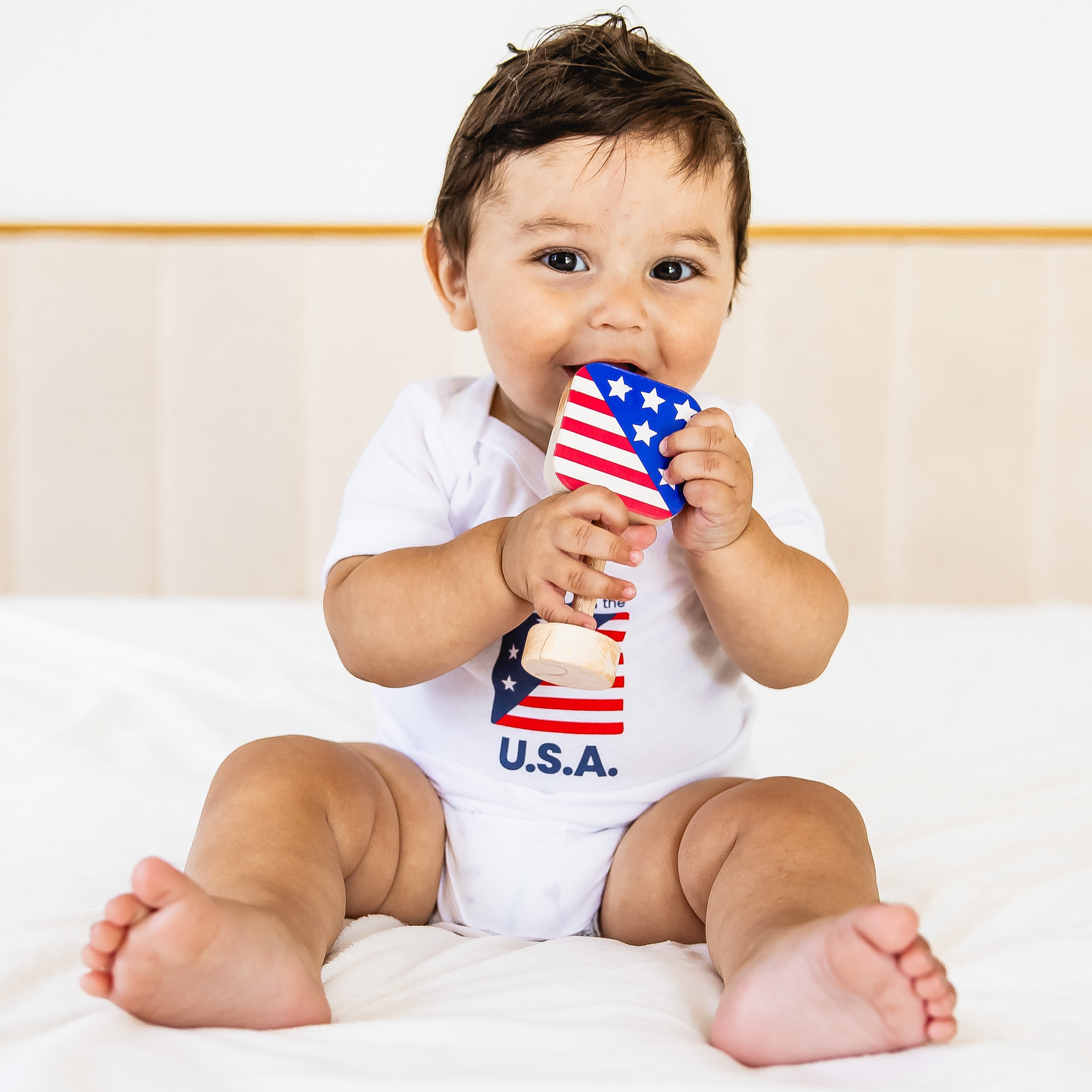 Baby holding a small American flag with 'U.S.A.' text on a white background