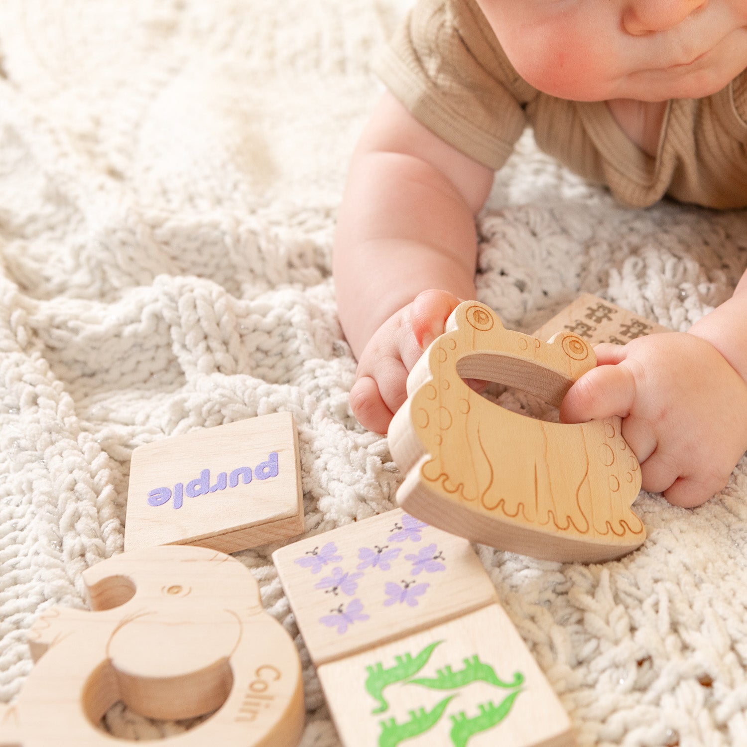 A baby is holding a wooden frog teether and playing with the Montessor-inspired learning tiles.
