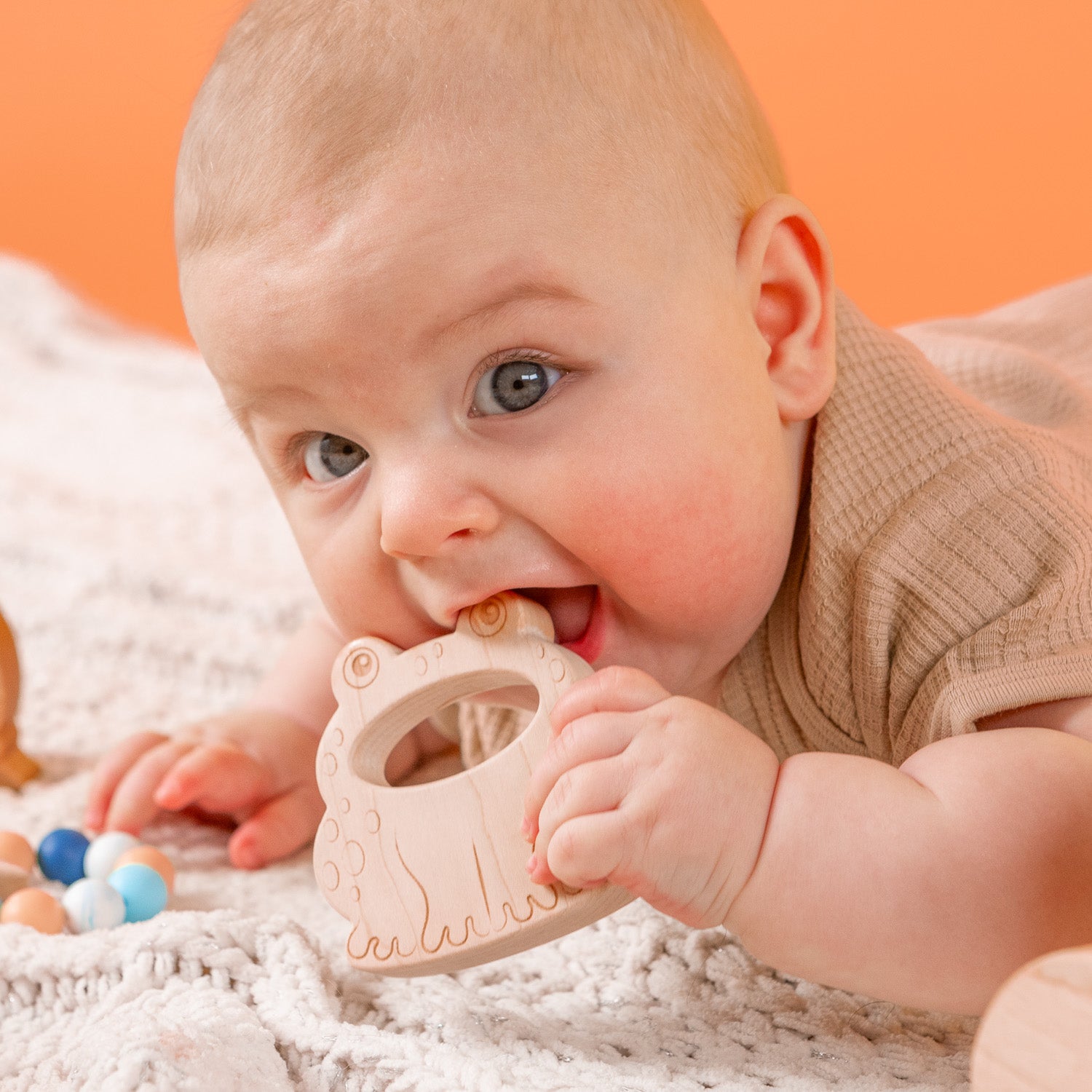 Baby lying on tummy with a wooden teether in his mouth.