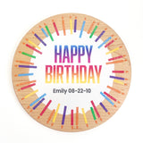 A round wooden plaque with a white center reading 'HAPPY BIRTHDAY' in rainbow gradient letters, personalized with the name 'Emily' and date '08-22-10' in black text. The wood border is decorated with colorful illustrations of birthday candles, all set against a plain white background.