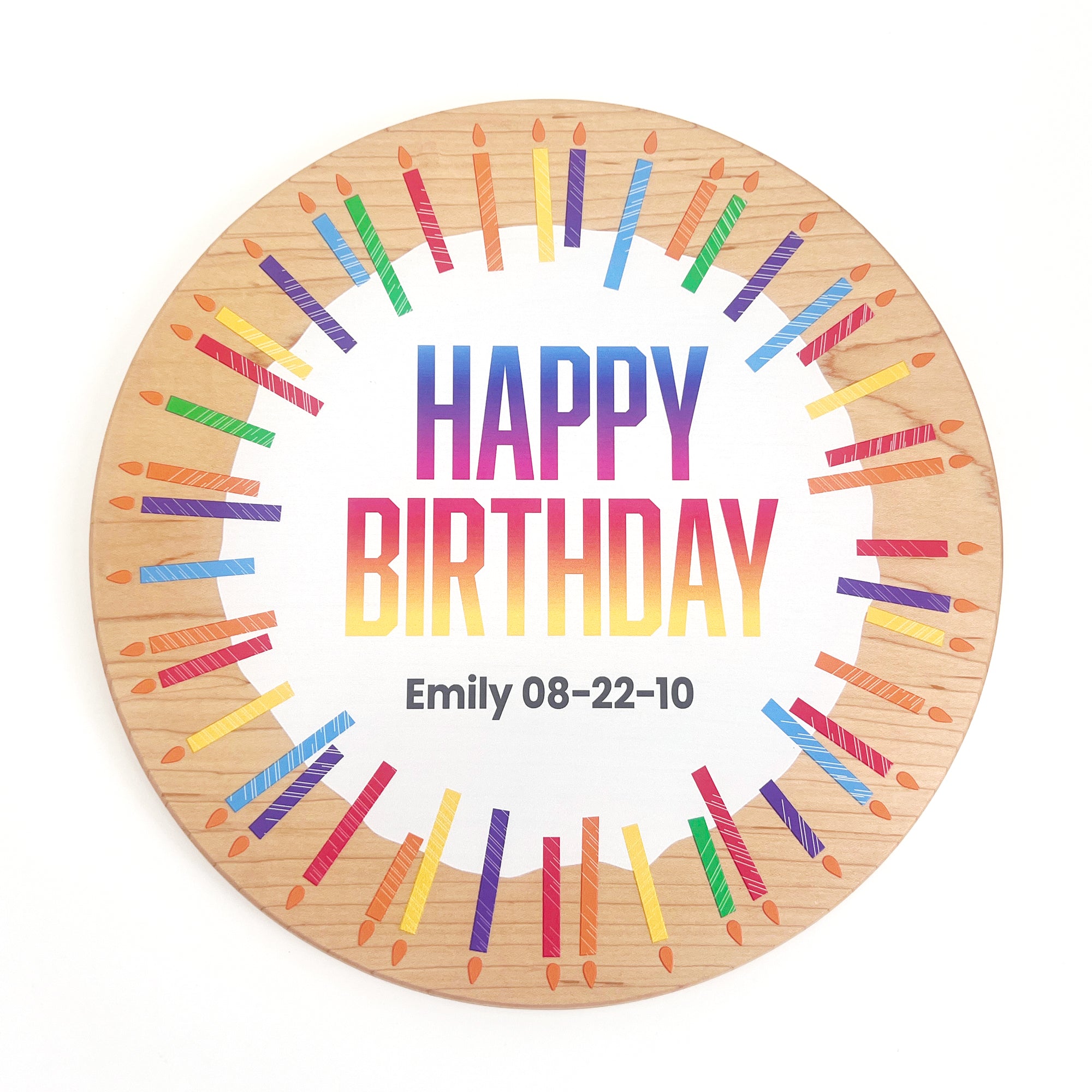 A round wooden plaque with a white center reading 'HAPPY BIRTHDAY' in rainbow gradient letters, personalized with the name 'Emily' and date '08-22-10' in black text. The wood border is decorated with colorful illustrations of birthday candles, all set against a plain white background.