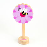 A wooden rattle with a flower and bee top, a long wooden dowel for grasping and a small base with the word "flower" spelled out. 
