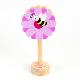 A wooden rattle with a flower and bee top, a long wooden dowel for grasping and a small base with the word "flower" spelled out. 