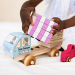 Child playing with a wooden toy ice cream truck and colorful blocks.
