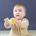 An cute baby holding up the Montessori-inspired learning tiles with green dinosaurs and yellow chicks on them. 