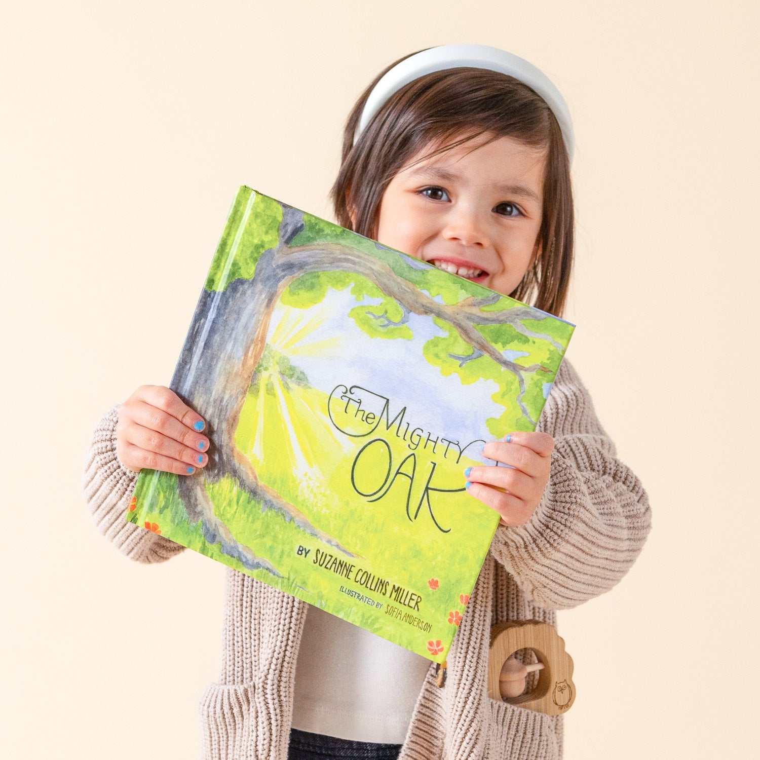 A girl is holding up The Mighty Oak book by Suzanne Collins Miller.