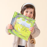 A gir is holding up The Mighty Oak by Suzanne Collins Miller with the The Mighty Oak rattle in her pocket.