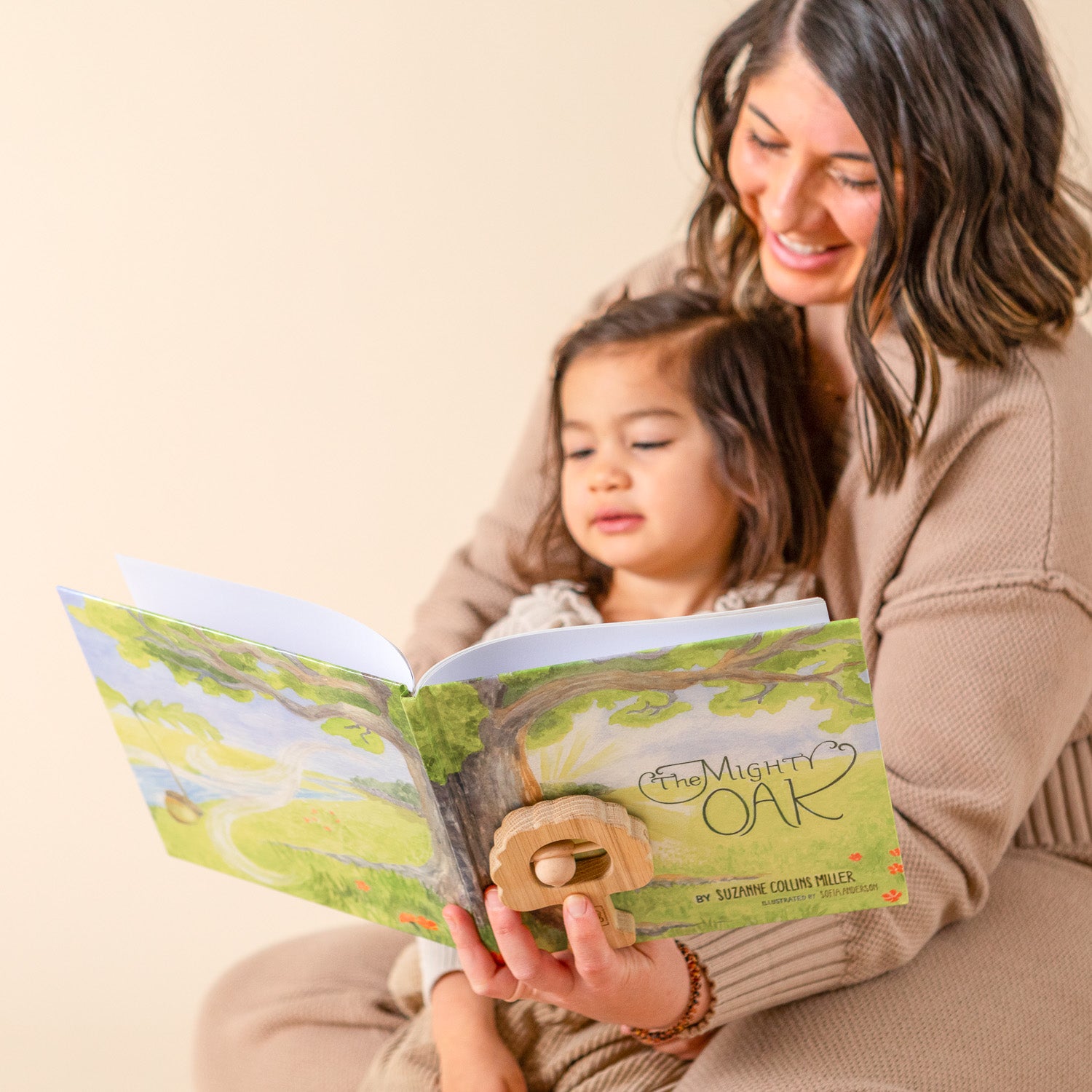 A mother is reading The Mighty Oak book to her daughter, who is sitting in her lap. 