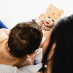 Baby wearing a bear hat looking at itself in a mirror with a woman holding it.