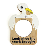 A white stork with yellow beak holding a circular mirror with "Look what the stork brought" written in black lettering across the bottom.