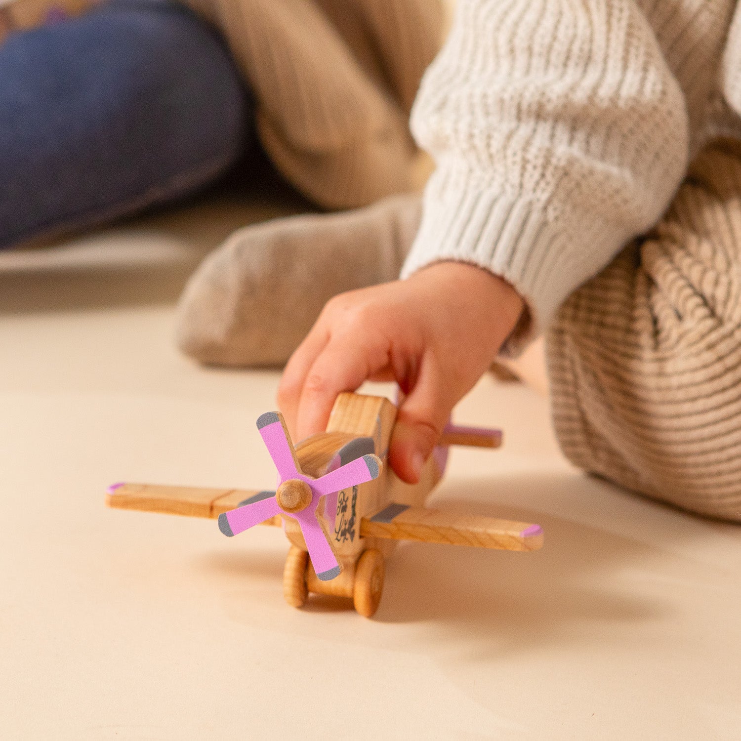 A little hand holding a wooden airplane with pink accents.