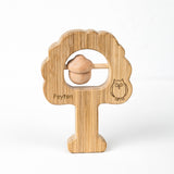 A wooden oak tree rattle with a rounded handle and a small bell attached to a wooden ring, engraved with the name 'Peyton' and an owl illustration.