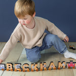 A boy playing with a magnetic train that spells out his name "Beckham".