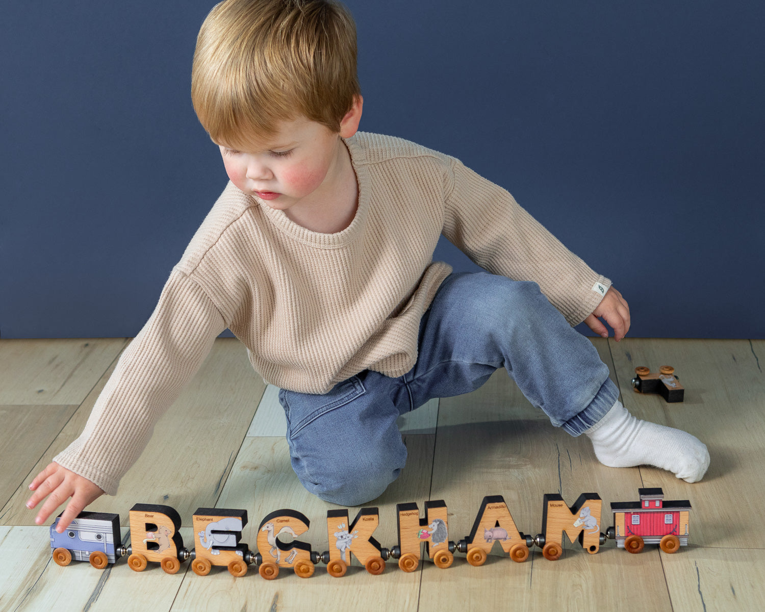 A boy playing with a magnetic train that spells out his name "Beckham".