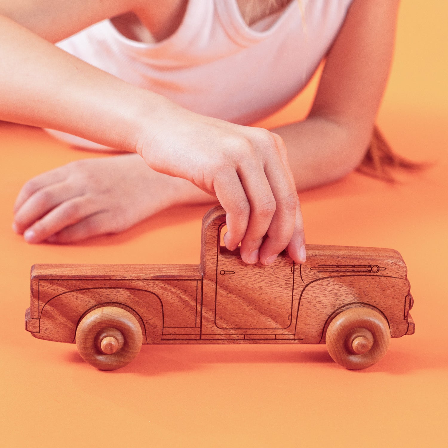 Girl playing on the floor holding the top of a wooden pickup truck.