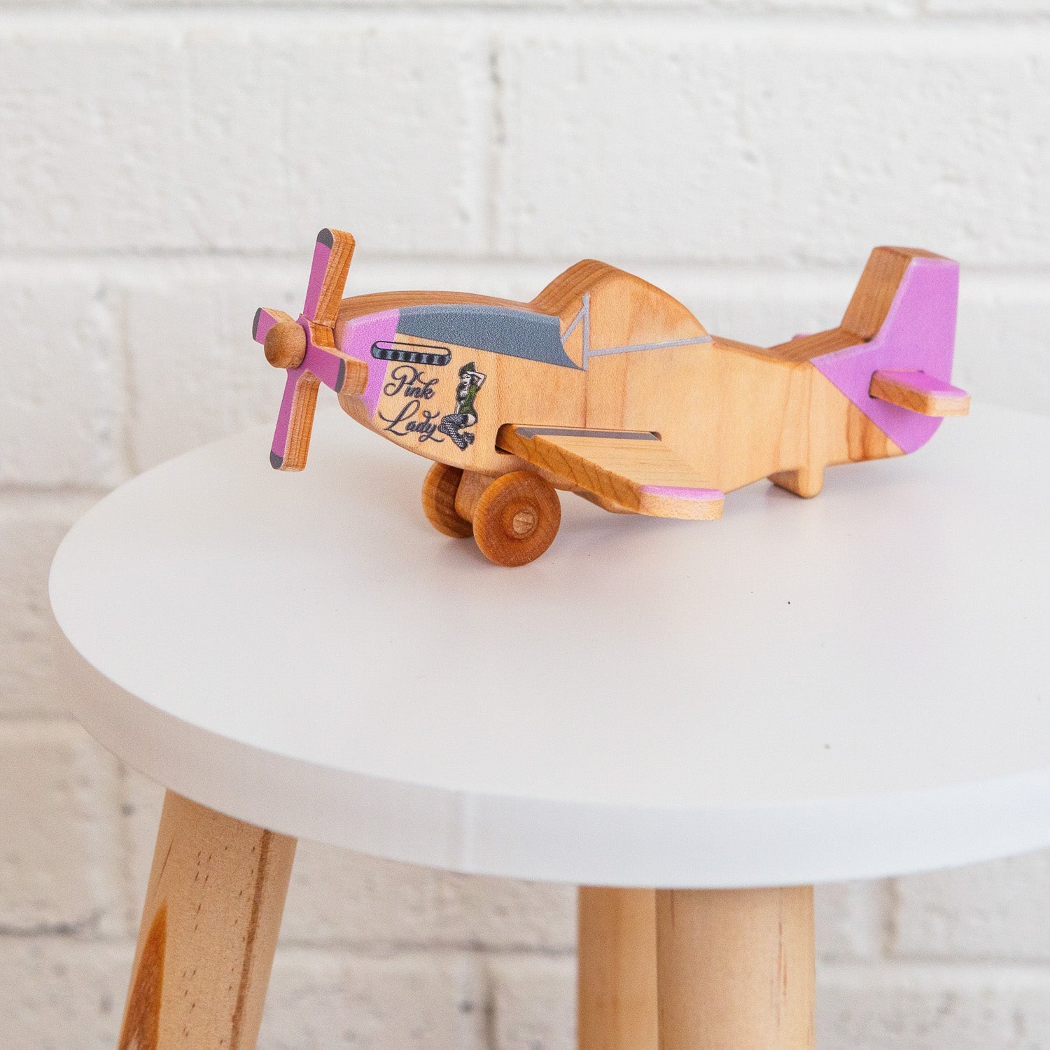 A pink wooden airplane siting on a stool.