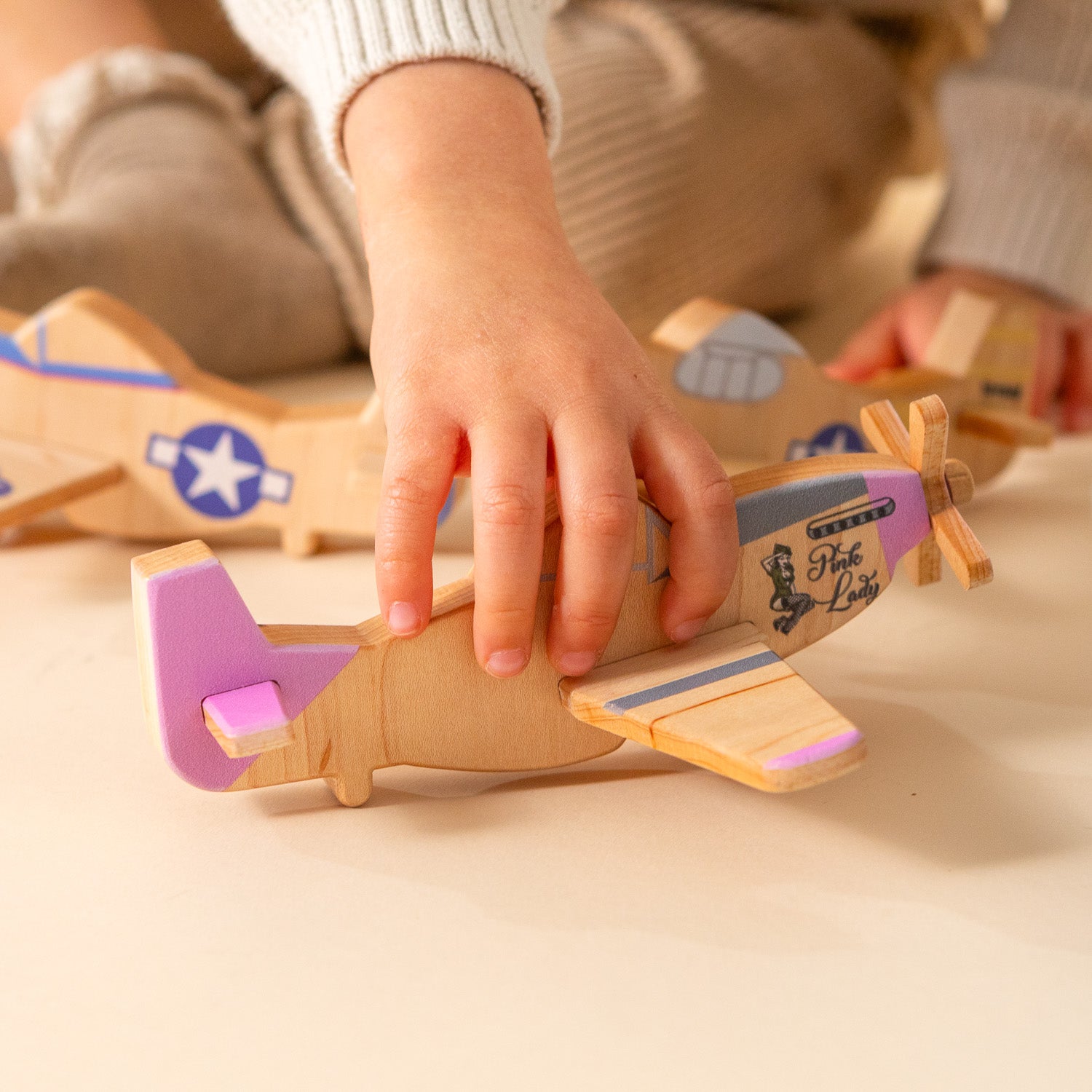Child playing with pink wooden airplane.