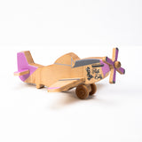 A hand-carved wooden airplane toy with pink accents on the wings and propeller, and a beige body.