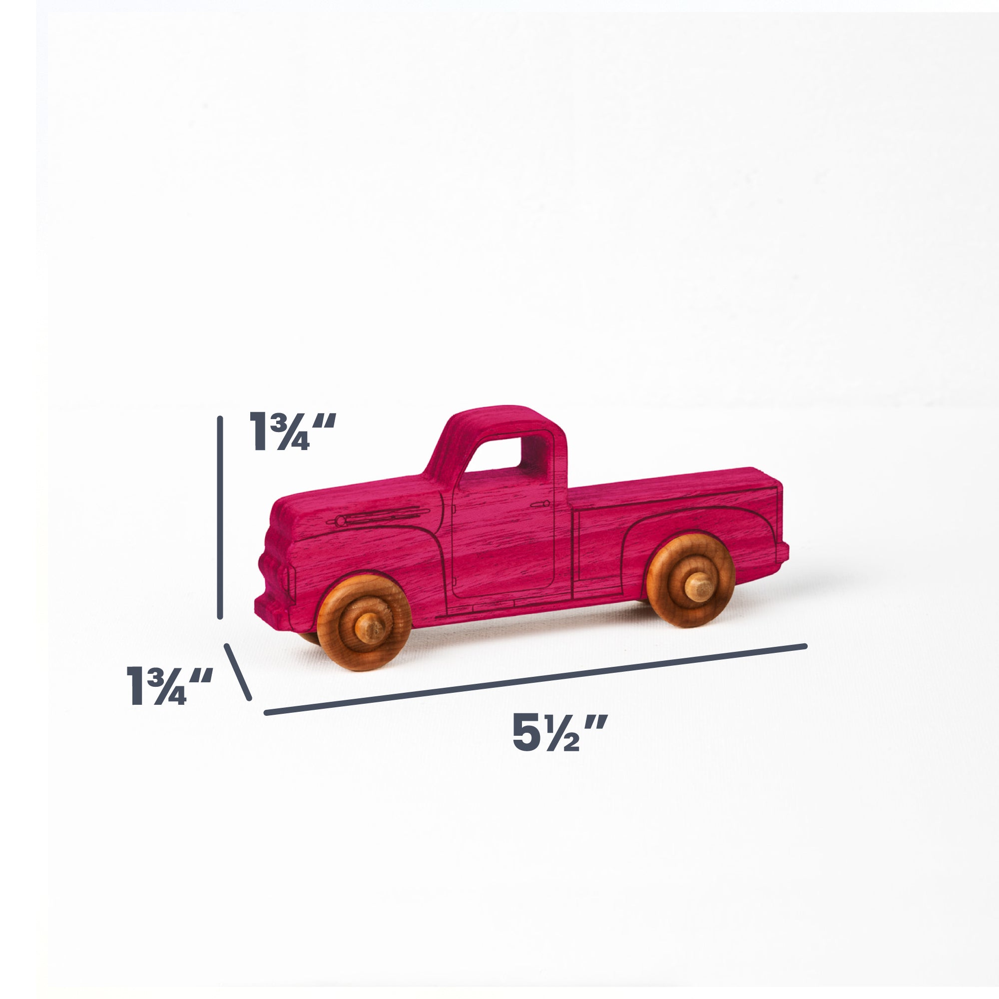 A small wooden toy pickup truck in bright pink with natural wood wheels, shown on a white background with dimension lines and labels indicating height of 1 3/4 inches, depth of 1 3/4 inches, and length of 5 1/2 inches.