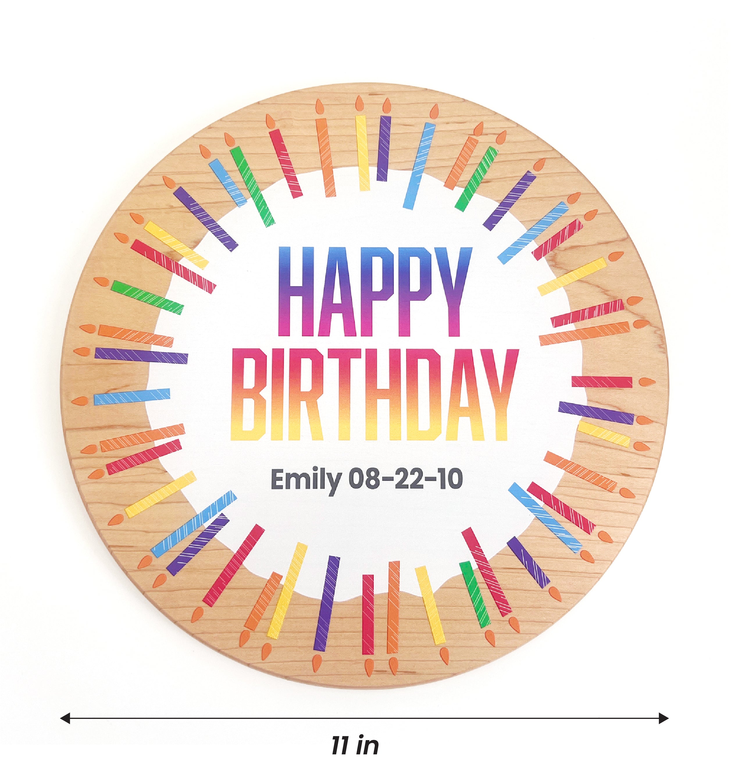 A round wooden birthday plaque with a natural wood grain border, featuring a white center with the text 'HAPPY BIRTHDAY' in a rainbow gradient and the name 'Emily 08-22-10' printed below. Colorful painted candles in a circular pattern surround the text.