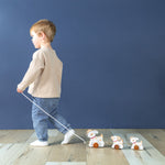 A boy holding a string pulling three wooden dogs connected on wheels behind him.