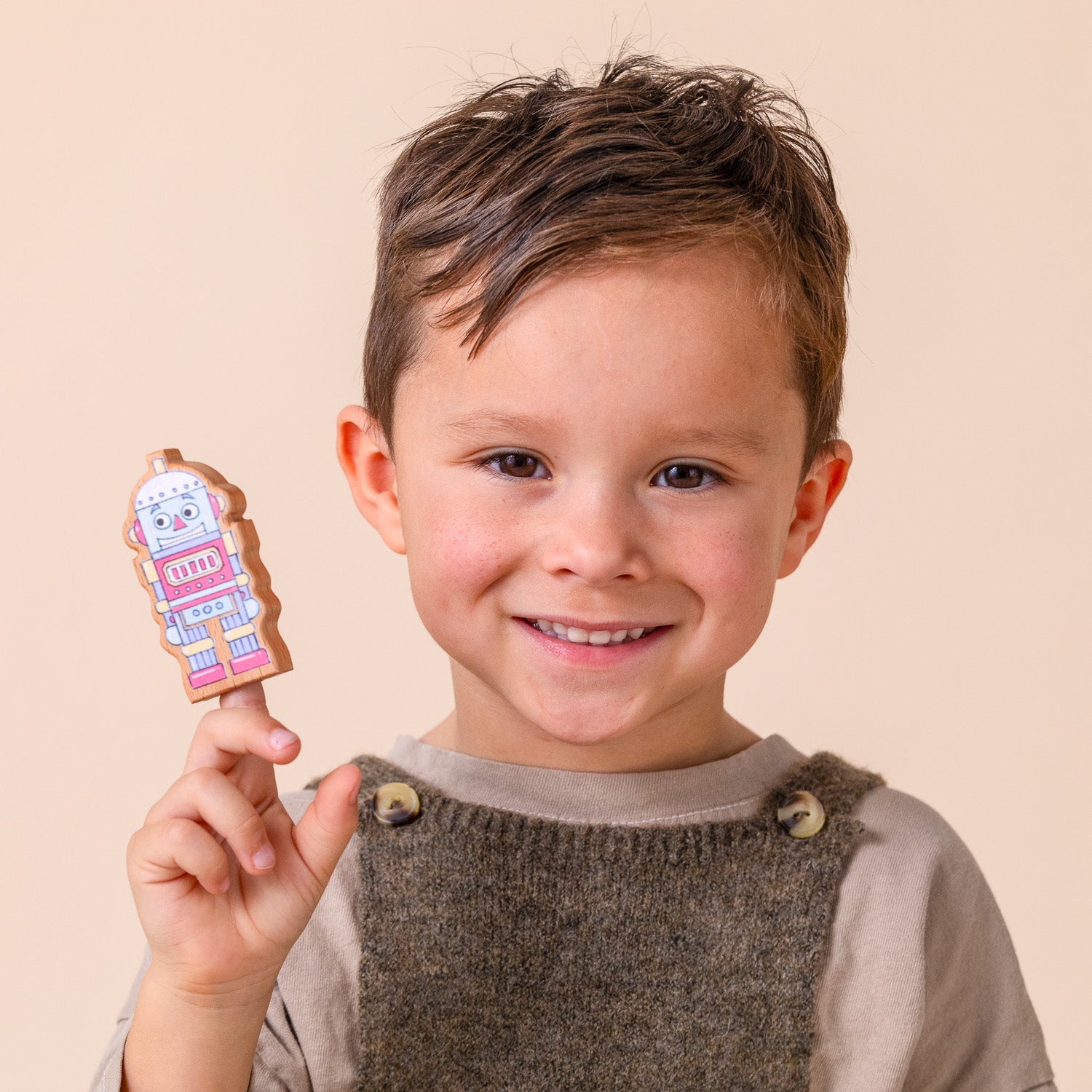 A boy holding up a wooden robot finger puppet.