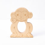 A wooden teether in the shape of a smiling monkey with a hole in the center for teething.