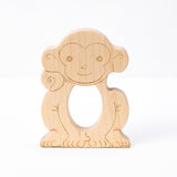 A wooden teether in the shape of a smiling monkey with a hole in the center for teething.