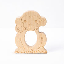 A wooden teether in the shape of a smiling monkey with a hole in the center for teething.