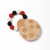 A silicone bead teether designed to look like a ladybug, with a wooden texture and red, white, and black beads attached to it.