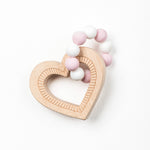 A heart-shaped teether made of silicone beads and wooden textures, primarily in pink and white colors.