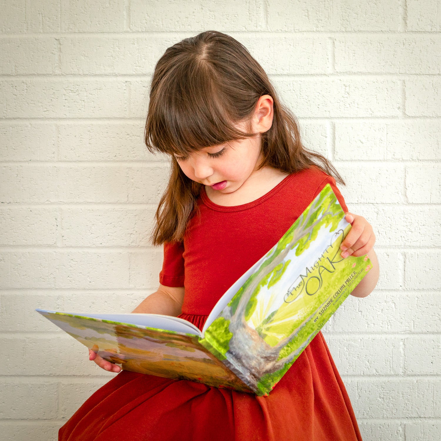 A girl in a red dress reading The Might Oak book.