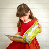A girl in a red dress reading The Might Oak book.