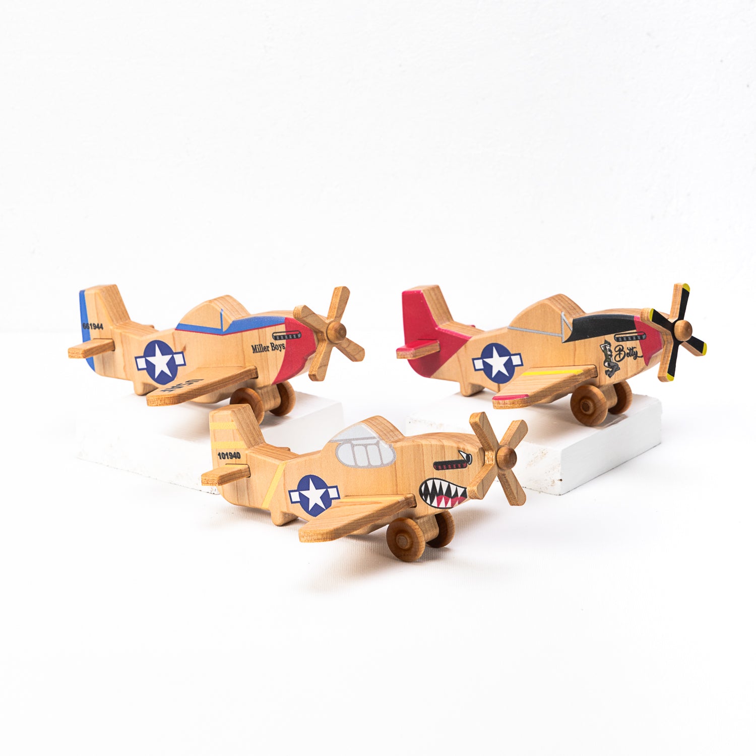 A set of three hand-carved wooden airplanes with classic P-51 Mustang designs, featuring vibrant colors and propellers.