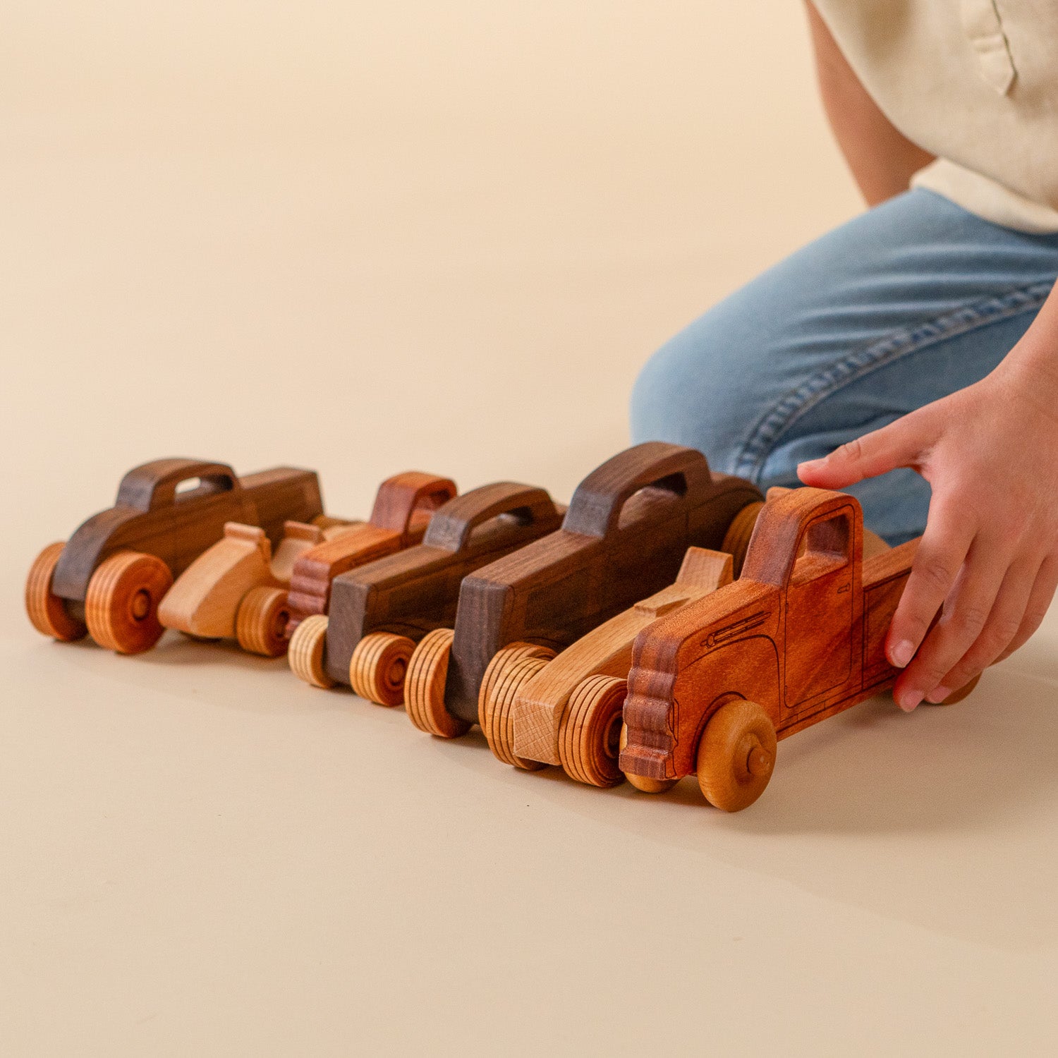 Child playing with wooden vehicles all lined up.