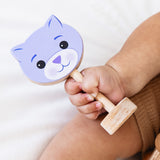 Child's hand holding a wooden toy with a cat face design on a white background