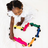 Child playing with colorful wooden toy cars on a white surface