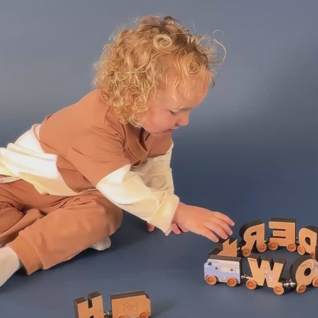 A boy playing with a magnetic letter train that spells out wonder with a blue diesel engine.