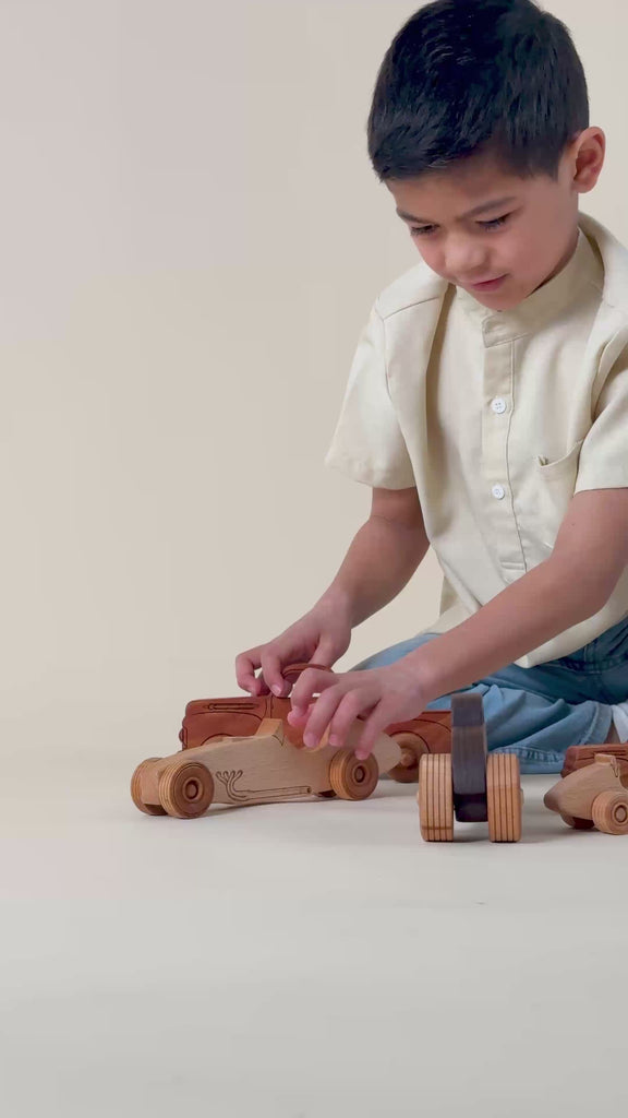 A boy playing with a wooden race car and a 1950s pickup truck.