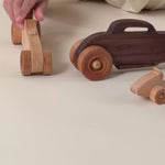 A boy rolling a wooden race car on the ground. 